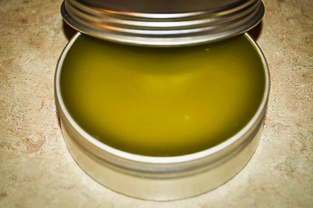 green herbal salve in a silver tin with the lid propped on the edge