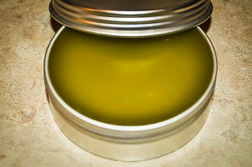 green herbal salve in a silver tin with the lid propped on the edge